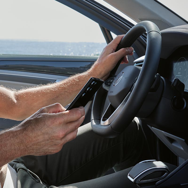 Eine Person bedient ein Smartphone, das mit den digitalen Funktionen eines VW Fahrzeugs vernetzt ist.