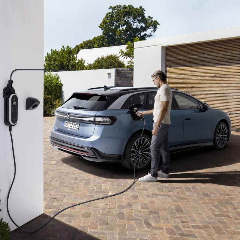 Eine Person lädt ein VW ID. Fahrzeug mit einer Wallbox auf einem Privatgrundstück.